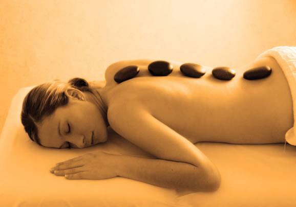 A lady lying face down on a massage table with hot stones aligned on her spine